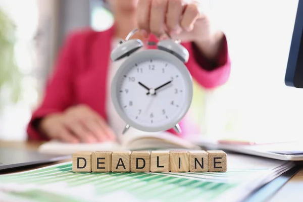 Business woman with alarm clock in hand and text deadline on cubes. Time management techniques concept