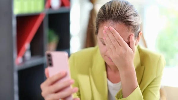 Sad girl upset reading bad news in a mobile message on smartphone in office at table. Chatting and bad news