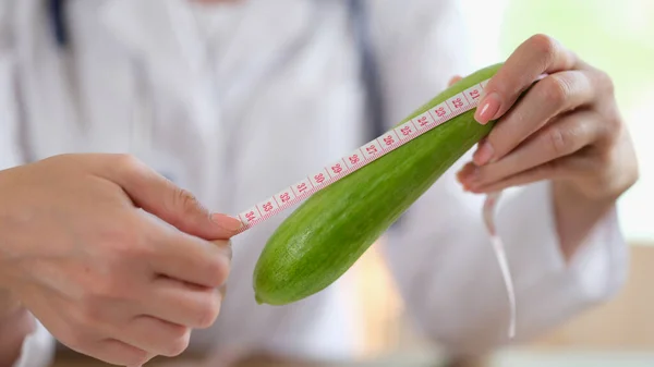 Doctor urologist and andrologist holds a centimeter of fresh cucumber. Measuring vegetables or male organ disease in men