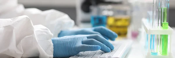 Hands of scientist in gloves works on keyboard in laboratory. Scientific research and data concept