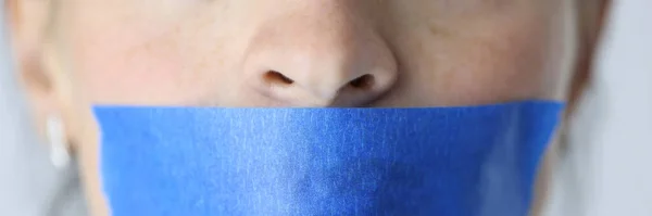 Woman mouth is sealed with blue tape. Silence and domestic violence concept