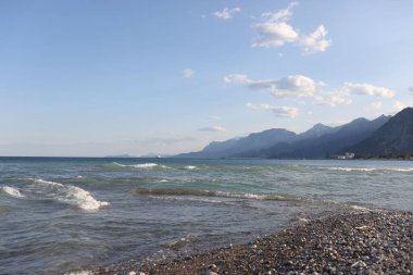Dalgalı deniz ve beyaz köpüklü çakıl taşı plajına yakın çekim. Dağ manzarası. Resimli deniz kıyısı. Yaz zamanı konsepti
