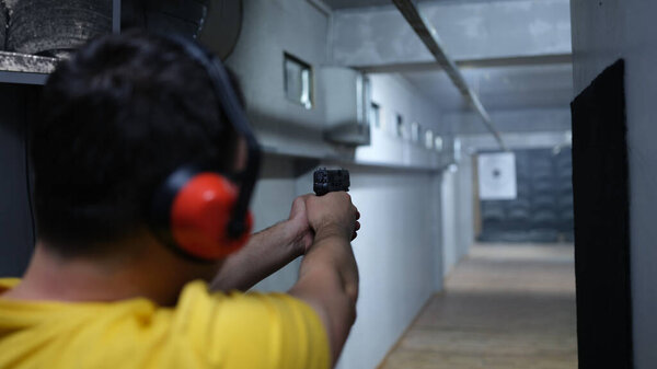 Close-up of man shooter in headphones shooting at target. Shooting practicing with gun in rifle range. Extreme hobby concept