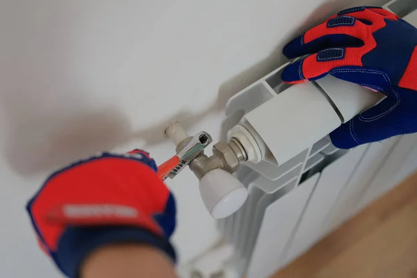 Close-up of man plumber installing heating radiator in apartment or house. Builder installs hot water central heating system. Repair concept