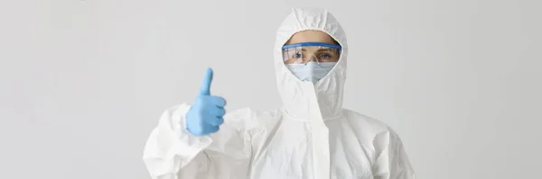 Doctor in protective suit holds thumbs up gesture. Qualitative fight against a pandemic of dangerous viral and bacterial infections concept