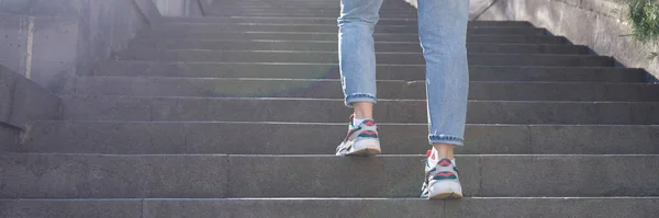 Athletic woman climbs stairs in sneakers with glare or sunspot. Daily city walks for health concept