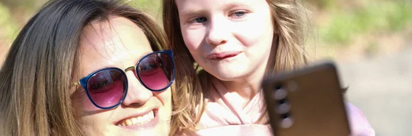 Mom and daughter take selfie on phone on sunny day. Family photos and summer walks concept