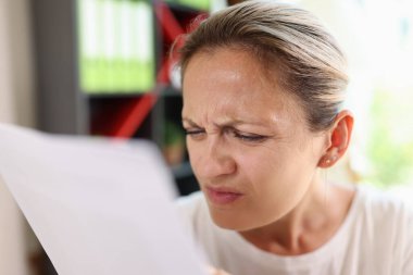 Daha net görebilmek için gözlerini kısarak gazete okumaya çalışan odaklanmış bir kadının portresi. Görme sorunları nedeniyle metni görmekte zorlanan kadın