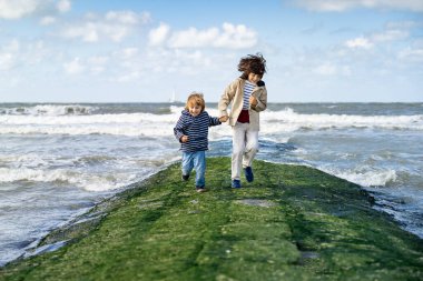 İki kardeş Kuzey Denizi 'nde bir dalgakıranda el ele tutuşuyorlar. Gülen çocuklar hafta sonunu Belçika 'nın deniz kıyısında geçiriyorlar Knokke. Kardeşler dostluğu.