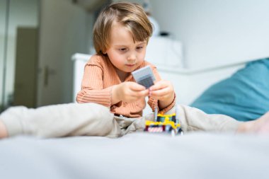 Küçük anaokulu çocuğu, odasındaki bir yatakta inşaatçıyla oynuyor. Çocuk karantina sırasında vakit geçiriyor. Oyun geliştirme kavramı, kopyalama alanı.