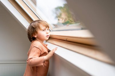 Üzgün sıkılmış çocuk pencereden içeri bakıyor. Bebek bir odada tek başına. Çocuk depresyonu konsepti.