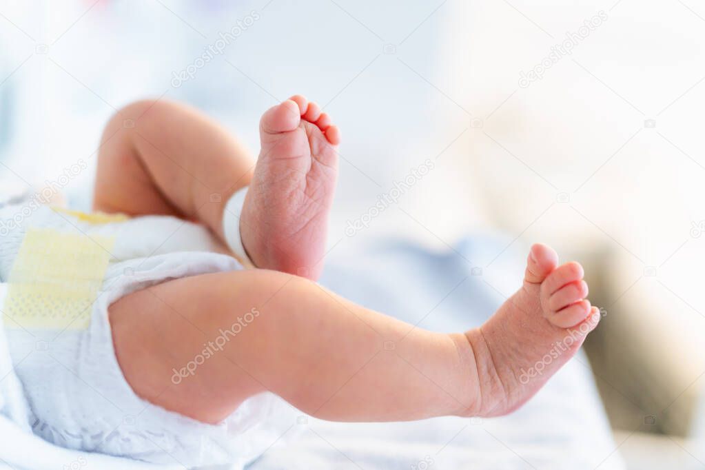 Newborn legs close up. Child birth, first day in hospital, newborn baby wearing diaper  in postpartum department.