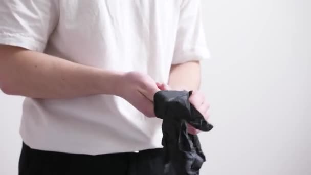 黒のジーンズと基本的な白いTシャツの男が取り、黒の手袋を着用します — ストック動画