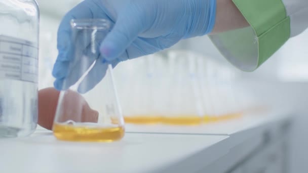 Químico poniendo vidrio de laboratorio con líquido amarillo en una mesa. Terminar el experimento — Vídeos de Stock