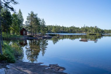 Stunning view of Serene and Reflecting Lake Tarnattvattnen and Remote hiking Resting Cottage in Skuleskogen National Park on a Summertime Evening with gorgeous background of Slattdalsskrevan. 