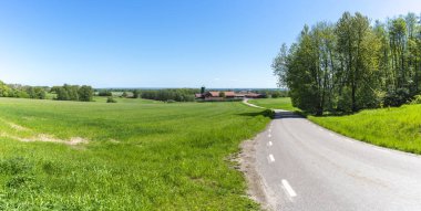 İlkbaharın sonlarında yeşil kırsal panoramik arazide virajlı köy yolu.