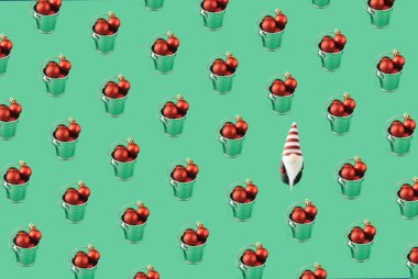 Noel ve Yeni Yıl 2022 kavramı. Noel ağacı için yeşil arka planda parlak kırmızı süslemelerle dolu gümüş bir kovayla bir Noel cücesi. asgari örüntü kavramı.