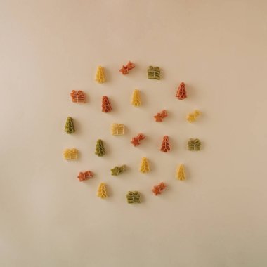 Noel ağacı, hediye ve kayan yıldız şeklinde yeşil, kırmızı ve sarı renkli makarna. Noel ve yeni yıl kutlamaları bej arkaplan üzerine en az fotokopi alanı kavramı.