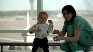 Toddler boy running from mom to camera in airport.