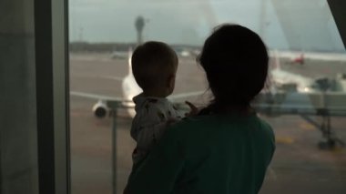 Silhouettes of mother and son looking at window in airport. Big aircraft.