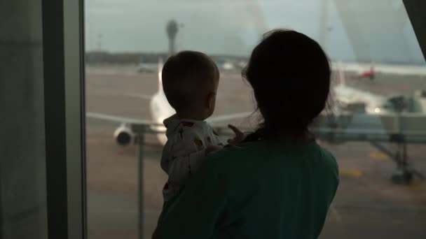 Silhouettes of mother and son looking at window in airport. Big aircraft. — Vídeos de Stock