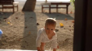 Toddler runs along the beach and climbs the steps into the hotel room and runs towards the camera. The concept of recreation with young children.