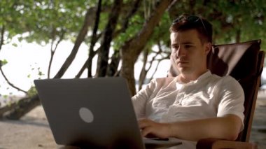 Young businessman tired and disappointed in his online work conversation and closes laptop at tropical vacation.