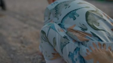 Sweet blond boy takes sand in hands having fun with family on beach at twilight. Parents with stroller and toddler enjoy vacation closeup slow motion