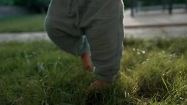 Sweet boy walks barefoot on lush grass growing in yard holding stick in hand. Toddler spends weekend in countryside on summer day closeup slow motion