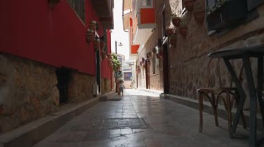 Mother and son walk on narrow shadowed street with old buildings on sunny day. Woman and toddler boy enjoy summer trip to ancient touristic town