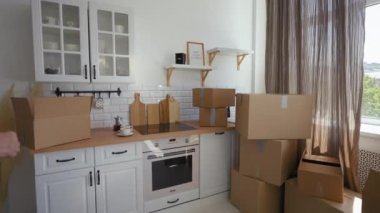 Happy senior man and woman show key to long-awaited flat at camera coming in kitchen. Elderly couple feels happy standing near paper boxes from POV to third party