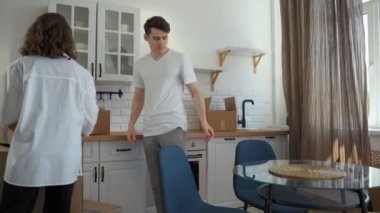 Kadın ve erkek tezgahın üstüne karton kutular koydular ve mutfaktaki cam masaya oturdular. Genç çift yeni eve bir şeyler getirdikten sonra ara veriyor.