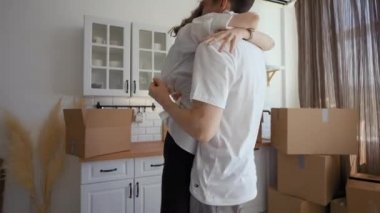 Man spins woman around and hugs in modern kitchen of new apartment against unpacked paper boxes. Happy young couple feels excited about relocation