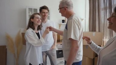 Senior father and mother gift new apartment to young married couple. Happy man and woman take key feeling thankful for present from parents standing in kitchen