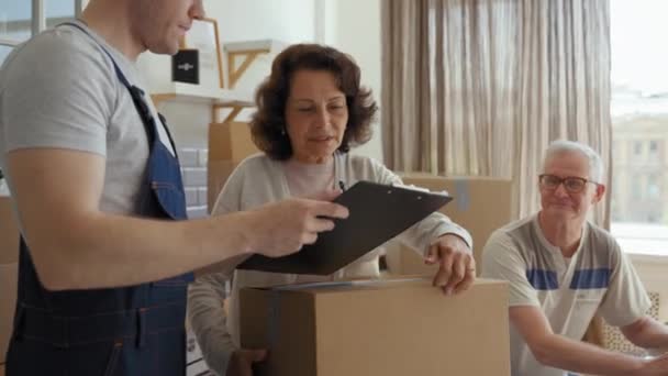 Courier Brings Cardboard Box New Apartment Elderly Couple Sitting Kitchen — Stockvideo