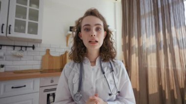 POV of therapist giving recommendations to patient on video call. Woman with stethoscope talks looking in camera sitting at kitchen table closeup