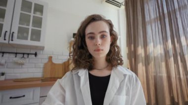 POV of young woman watching online courses on laptop making notes with pen. Female student sits at table in kitchen against window close view