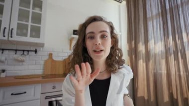 POV of cheerful woman talking on video call with friend. Young brunette lady sits at kitchen table at home and enjoys telling story close view