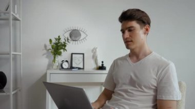Young man talks to manager on video call using laptop. Male freelancer discusses work conditions sitting in chair in modern living room closeup