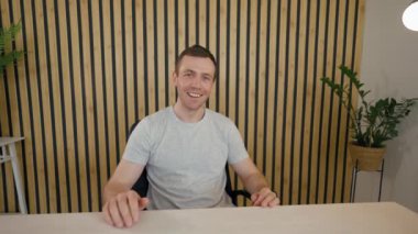 Young businessman talks at camera moving on to conversation with elderly customer. Men discuss project sitting at desk in office from POV to third party