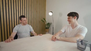 Man talks to colleague checking time on wristwatch and sitting at desk in modern office. Young employee turns looking in camera from third party to POV