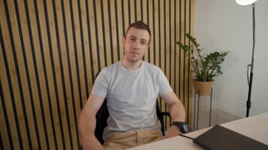 POV of young businessman listening to employee at online conference via video call. Man sits at desk in office looking in camera and waves head