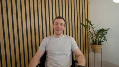 Man talks to friend on video call greeting colleague coming to office. Young employee sits on chair at desk distracting on workmate from POV to third party