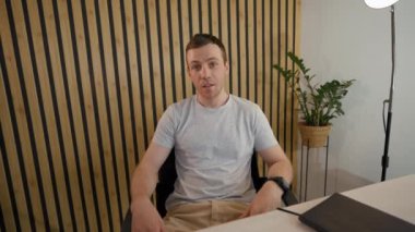 POV of business coach recording online lesson talking to camera. Young man teaches people remotely sitting at desk near pot-plant in modern office