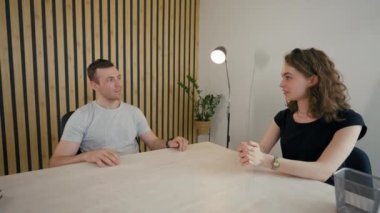 Businessman talks to lady employee applicant sitting at desk in office. Young man distracts from communication with lady turning to camera from third party to POV