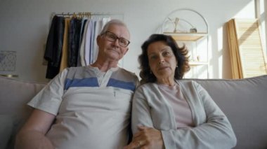 POV of elderly couple talking on video call via webcam with friends waving head. Senior man in glasses and woman sit on sofa in living room at home closeup