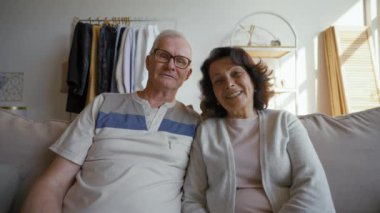 Senior man in glasses and woman enjoy communication on video call distracting on son coming to hug. Elderly people relax at home on sofa from POV to third party