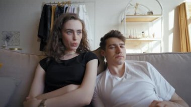 Woman tells funny story watching child photos in album resting on sofa with partner. Young couple sits in living room enjoying communication closeup