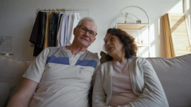 Happy senior man and woman enjoy online communication with old friends on video call. Son comes in room to hug elderly parents from POV to third party