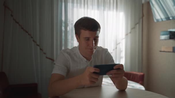 Young Man Plays Car Racing Smartphone Sitting Table Bright Window — Vídeos de Stock